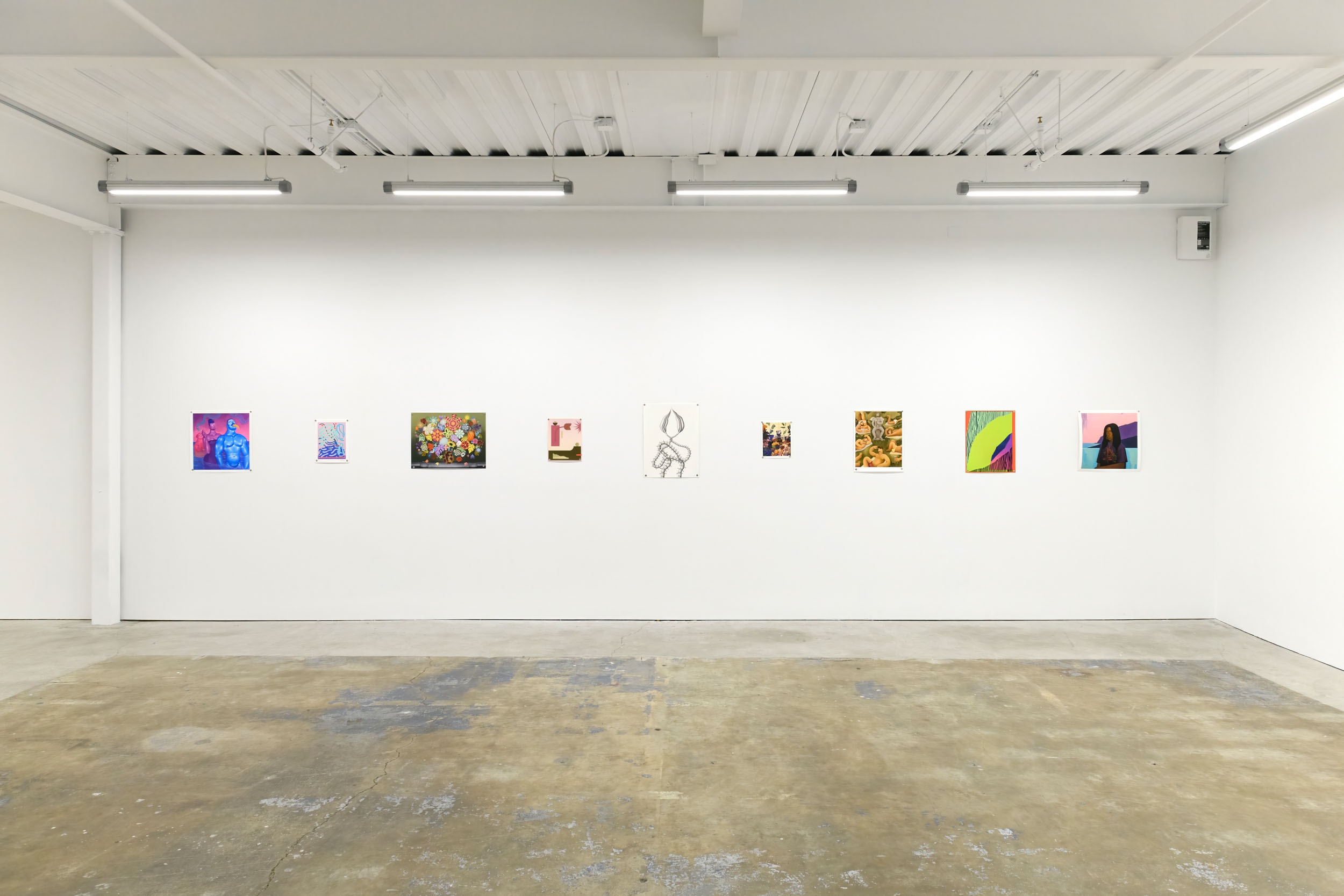 Prints of artworks on a white wall in an art gallery with fluorescent lighting. 