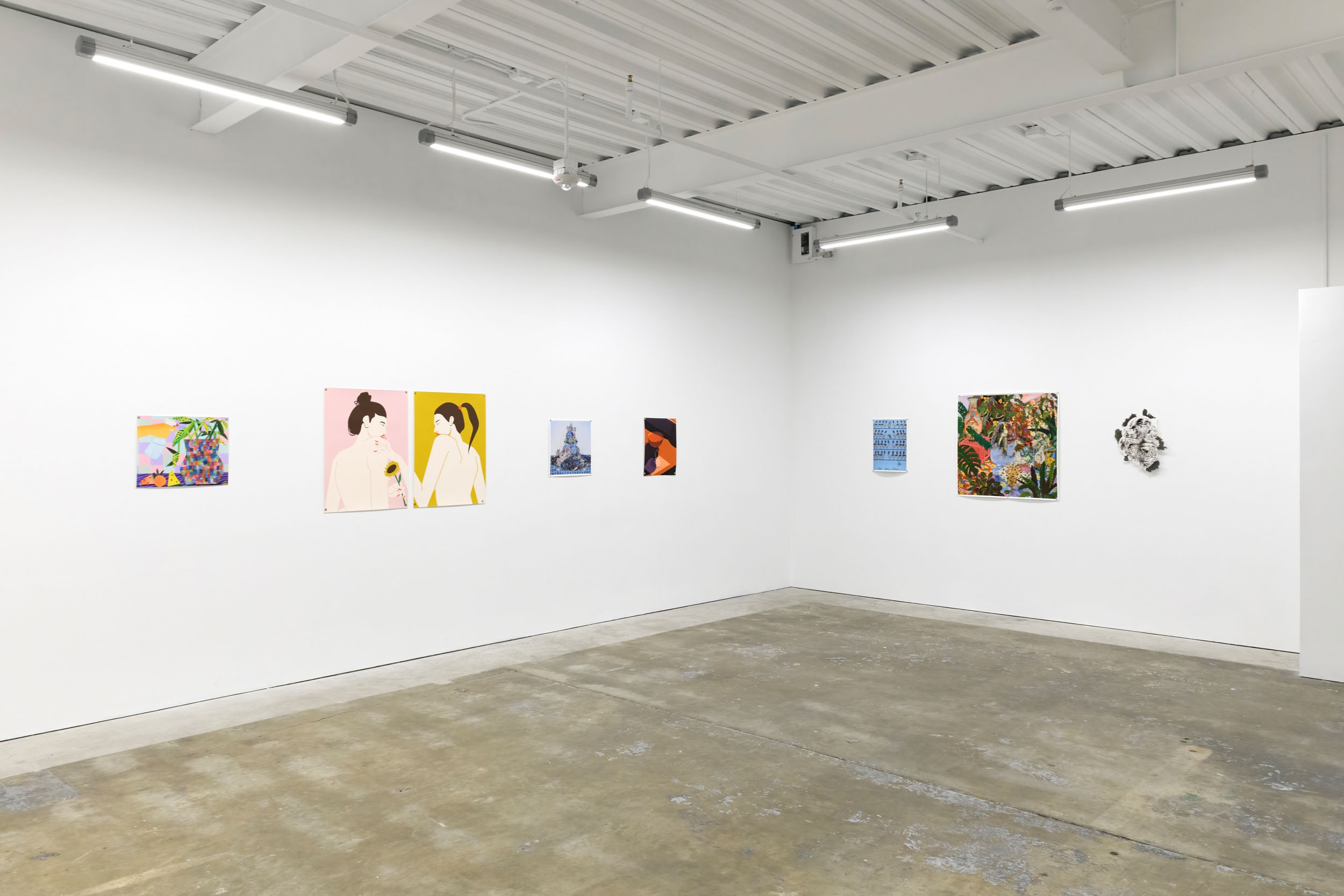 Prints of artworks on a white wall in an art gallery with fluorescent lighting. 